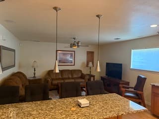 Spacious living room with leather seating, granite countertop bar, ceiling fan, and flat-screen television