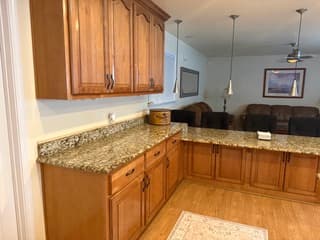 Kitchen counter area with granite surfaces and wooden cabinets opening to the living room