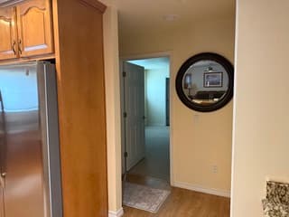 Hallway with stainless steel refrigerator, round decorative mirror, and view toward the bathroom